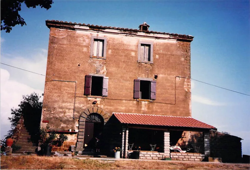 The Soriano nel Cimino farmhouse before restoration: bare stone and render, shuttered windows, an unfinished lean-to along one side