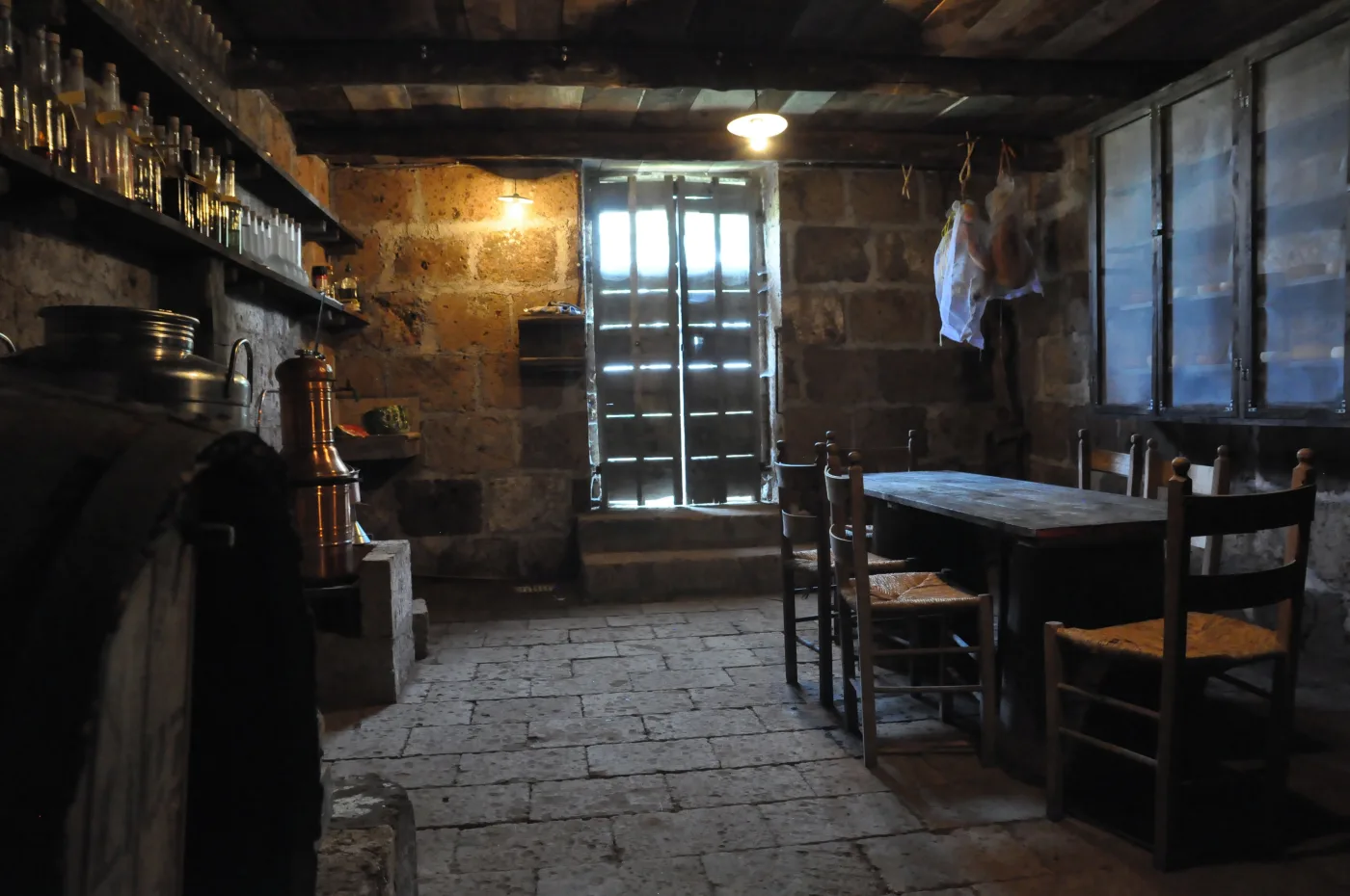 The stone cellar at Villa Eddarella: shelves of bottled liqueurs, a copper grappa still, prosciutti hanging from a beam, and a long wooden table